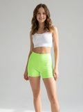 Driftly women's neon green polyester blend biker shorts with an elastic mid waist, styled with a white crop top in a minimalist studio setting.