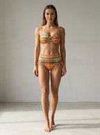 Driftly orange ethnic print high-waisted bikini set with ruched sides and secure straps, in a minimalist studio setting with soft window light.