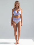 Driftly purple printed bikini top with adjustable straps, matching high-waisted bottoms, in a minimalist studio setting with soft window light.