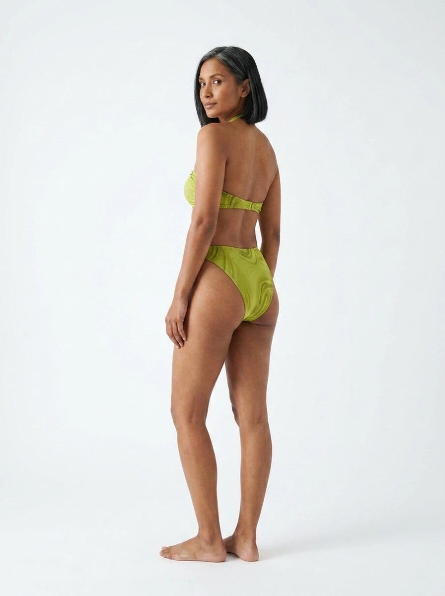 Woman wearing an olive green halter bikini set with bamboo swirl print, studio photography, back view