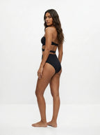 Woman wearing a black cut-out bikini set with cross-eyed overlay design, studio photography, back view