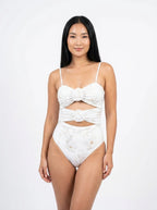 Woman wearing a white floral print swimsuit set with bow detail, studio photography, front view