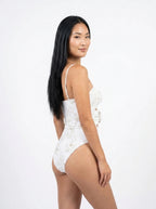 Woman wearing a white floral print swimsuit set with bow detail, studio photography, back view
