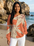 Woman wearing a peach leaf print long sleeve blouse with white trousers on a beach