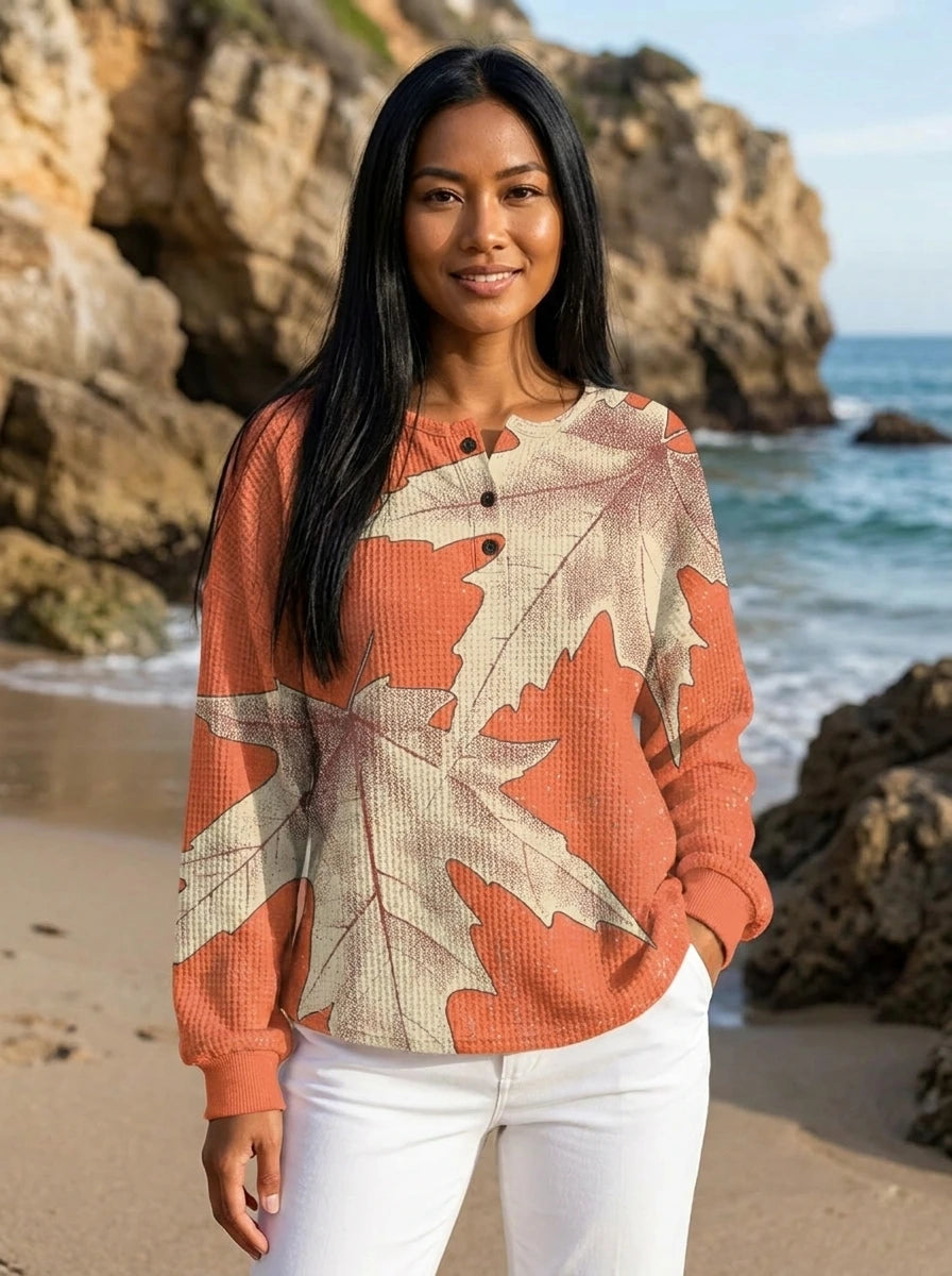 Woman wearing a peach leaf print long sleeve blouse with white trousers on a beach