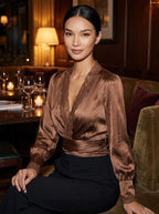 Woman wearing a bronze satin wrap blouse with lace trim in an elegant evening restaurant setting