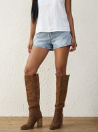 Woman wearing brown suede knee-high block heel boots with denim shorts, studio lifestyle photo