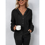 Woman wearing black hooded button-up cable knit cardigan holding a mug