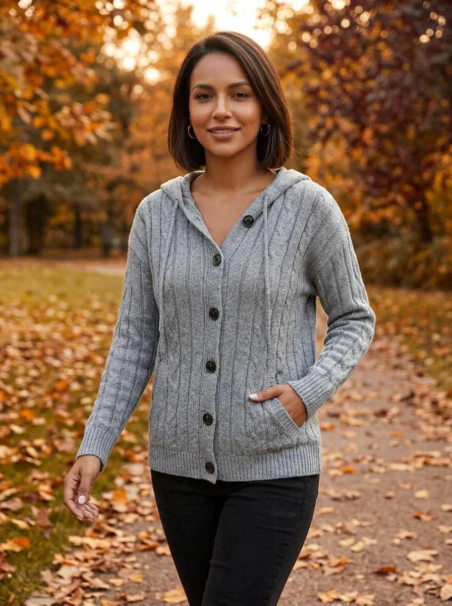Woman wearing grey hooded button-up cable knit cardigan, walking outdoors in autumn park