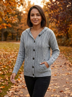 Woman wearing grey hooded button-up cable knit cardigan, walking outdoors in autumn park