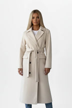 Woman wearing a cream double-breasted belted long coat - studio photo
