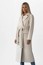 Woman wearing a cream double-breasted belted long coat - studio photo