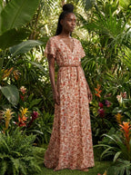 Woman wearing a rust and terracotta floral print boho maxi dress in a tropical garden