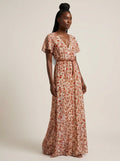 Woman wearing a rust and terracotta floral print boho maxi dress with flutter sleeves in a studio setting