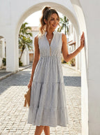 Woman wearing a white and grey pinstriped tiered midi dress on a sunny street beside a white archway