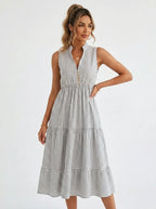 Woman wearing a white and grey pinstriped tiered midi dress in a bright studio setting