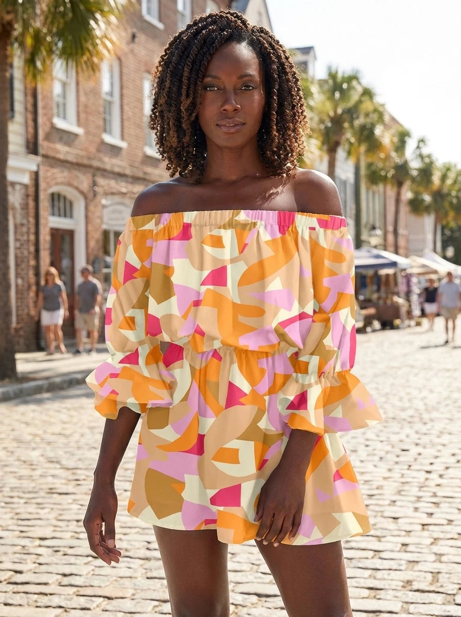 Woman wearing an orange and pink abstract geometric print off-shoulder mini dress on a sunny street