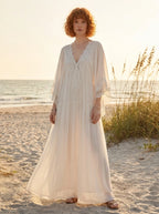 Woman wearing a white lace v-neck batwing sleeve chiffon maxi dress on a beach at golden hour