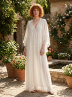 Woman wearing a white lace v-neck batwing sleeve chiffon maxi dress in a garden courtyard