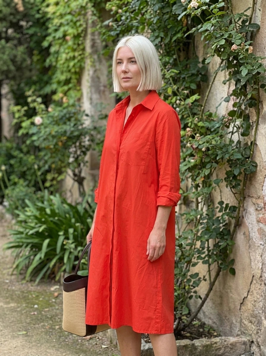 Woman wearing a red long sleeve midi dress standing near a garden wall