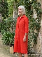 Woman wearing a red long sleeve midi dress standing near a garden wall