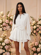 Woman wearing a white mini dress with a 3D rose belt at the waist in a studio setting
