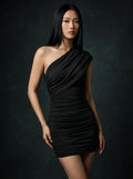 Woman wearing a black one-shoulder ruched mini dress with asymmetric neckline in a studio setting