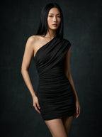 Woman wearing a black one-shoulder ruched mini dress with asymmetric neckline in a studio setting