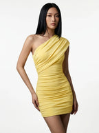 Woman wearing a yellow one-shoulder ruched mini dress with asymmetric neckline in a studio setting