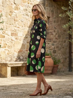 Woman in a black polka dot collared midi dress with green and white spots, three-quarter rolled sleeves.