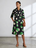 Driftly black polka dot collared midi dress with partial button front, three-quarter rolled sleeves, and side pockets, in a minimalist studio setting with soft window light.