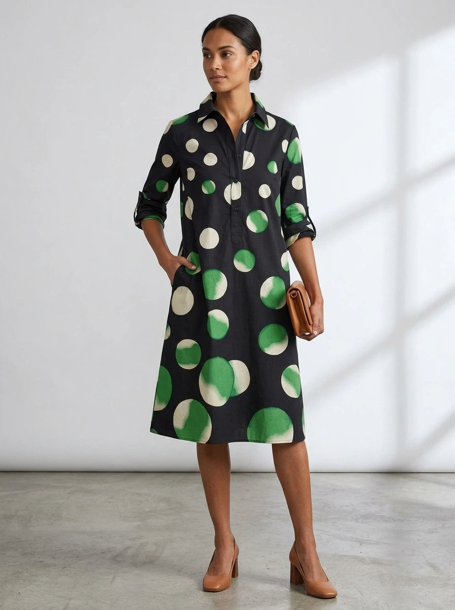 Driftly black polka dot collared midi dress with partial button front, three-quarter rolled sleeves, and side pockets, in a minimalist studio setting with soft window light.