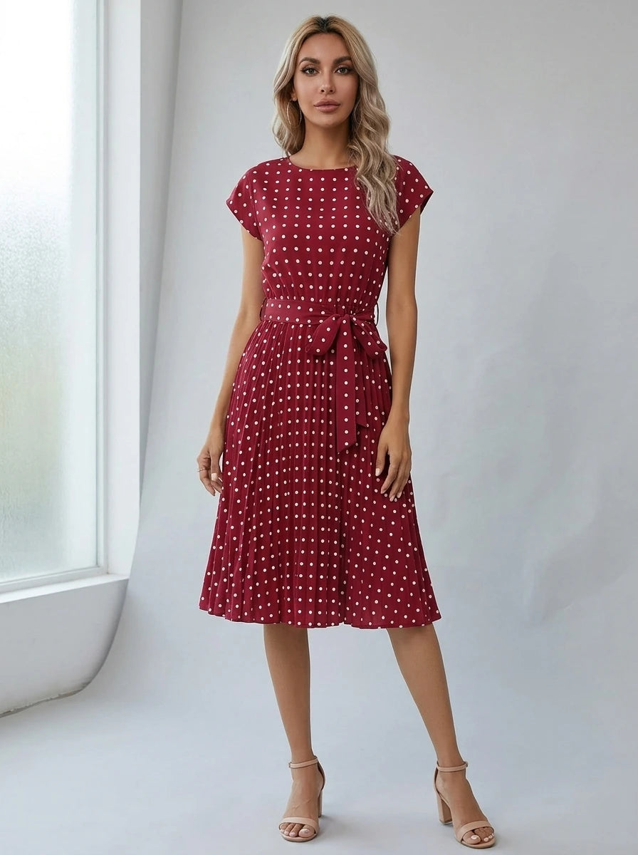 Driftly burgundy polka dot pleated midi dress with cap sleeves and a self-tie waist belt, in a minimalist studio setting with soft window light.