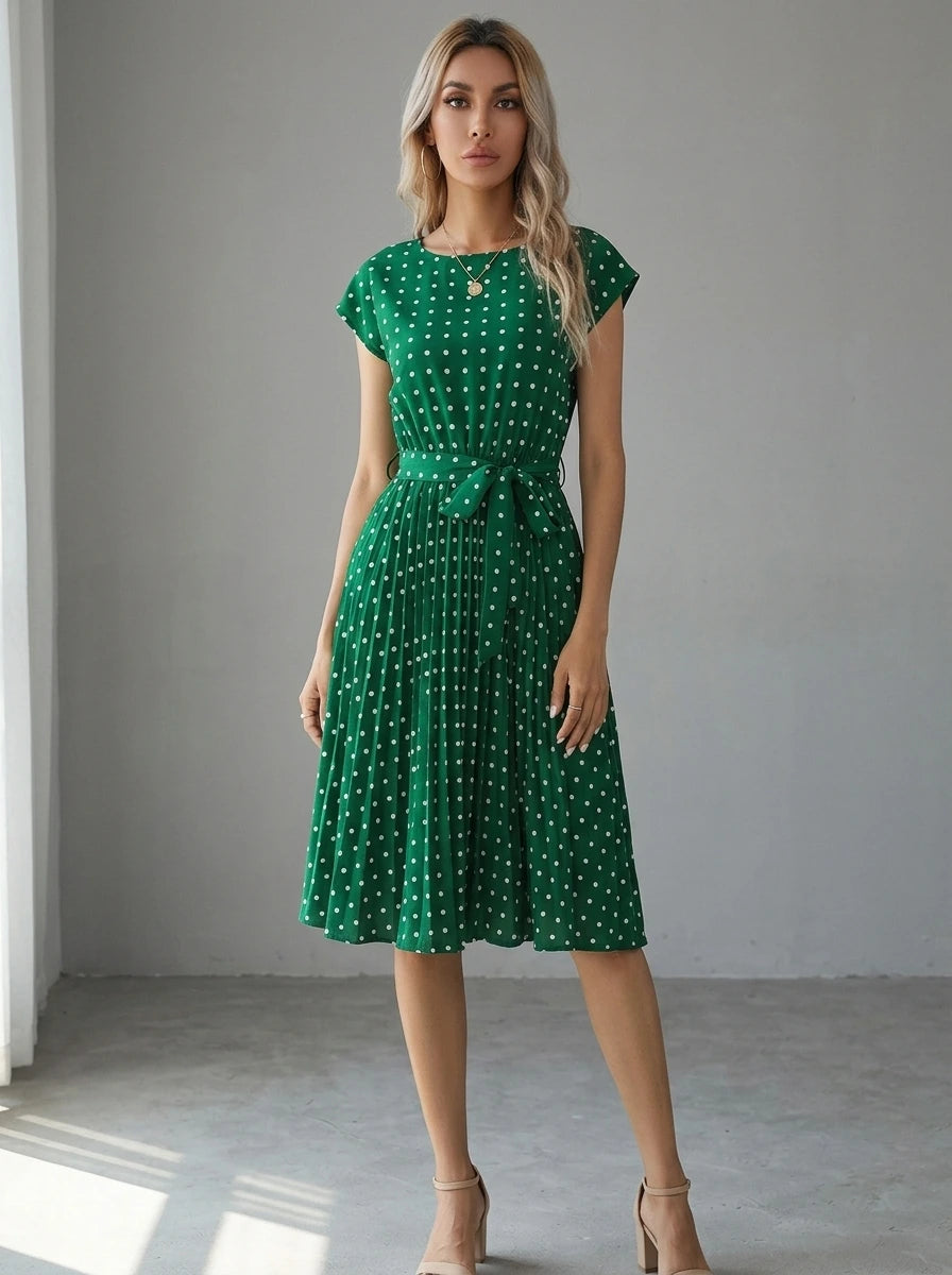 Driftly green polka dot pleated midi dress with cap sleeves and a self-tie waist belt, in a minimalist studio setting with soft window light.