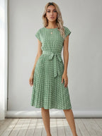 Driftly mint green polka dot pleated midi dress with cap sleeves and a self-tie waist belt, in a minimalist studio setting with soft window light.