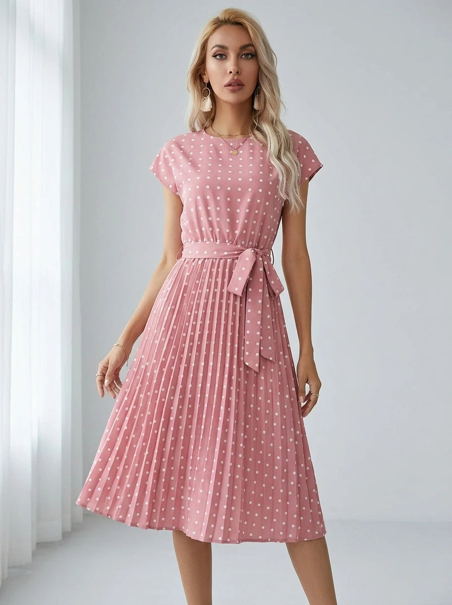 Driftly pink polka dot pleated midi dress with cap sleeves and a self-tie waist belt, in a minimalist studio setting with soft window light.