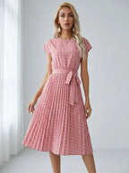 Driftly pink polka dot pleated midi dress with cap sleeves and a self-tie waist belt, in a minimalist studio setting with soft window light.