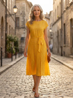 Driftly yellow polka dot pleated midi dress with cap sleeves and a self-tie waist belt, on a European street at golden hour.
