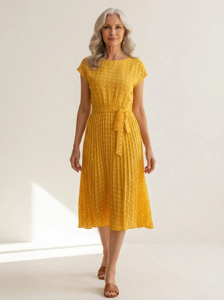 Driftly yellow polka dot pleated midi dress with cap sleeves and a self-tie waist belt, in a minimalist studio setting with soft window light.