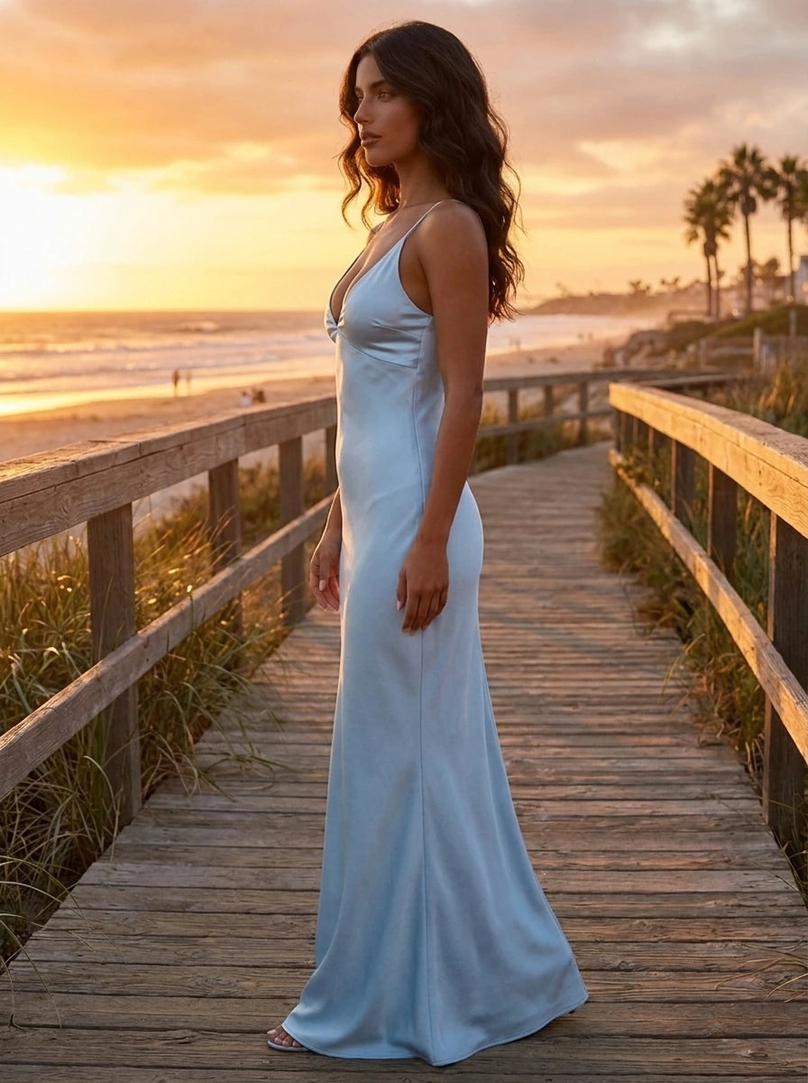 Woman wearing a light blue satin maxi dress with thin straps on a beach boardwalk at sunset