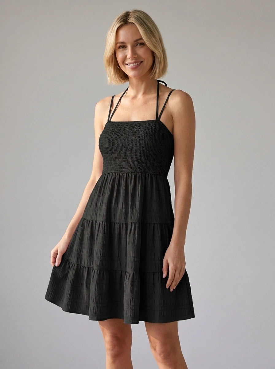 Woman wearing a black smocked tiered mini dress in a studio setting