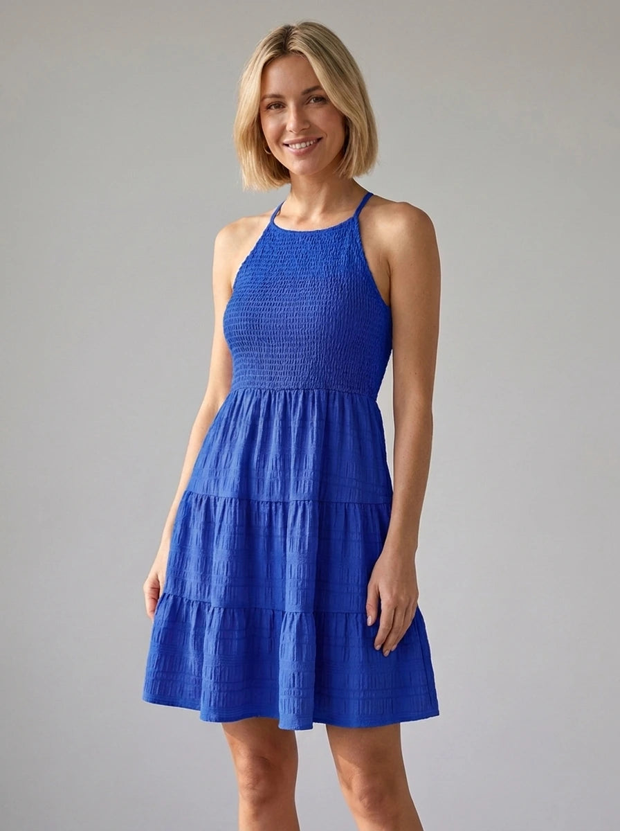 Woman wearing a blue smocked tiered mini dress in a studio setting