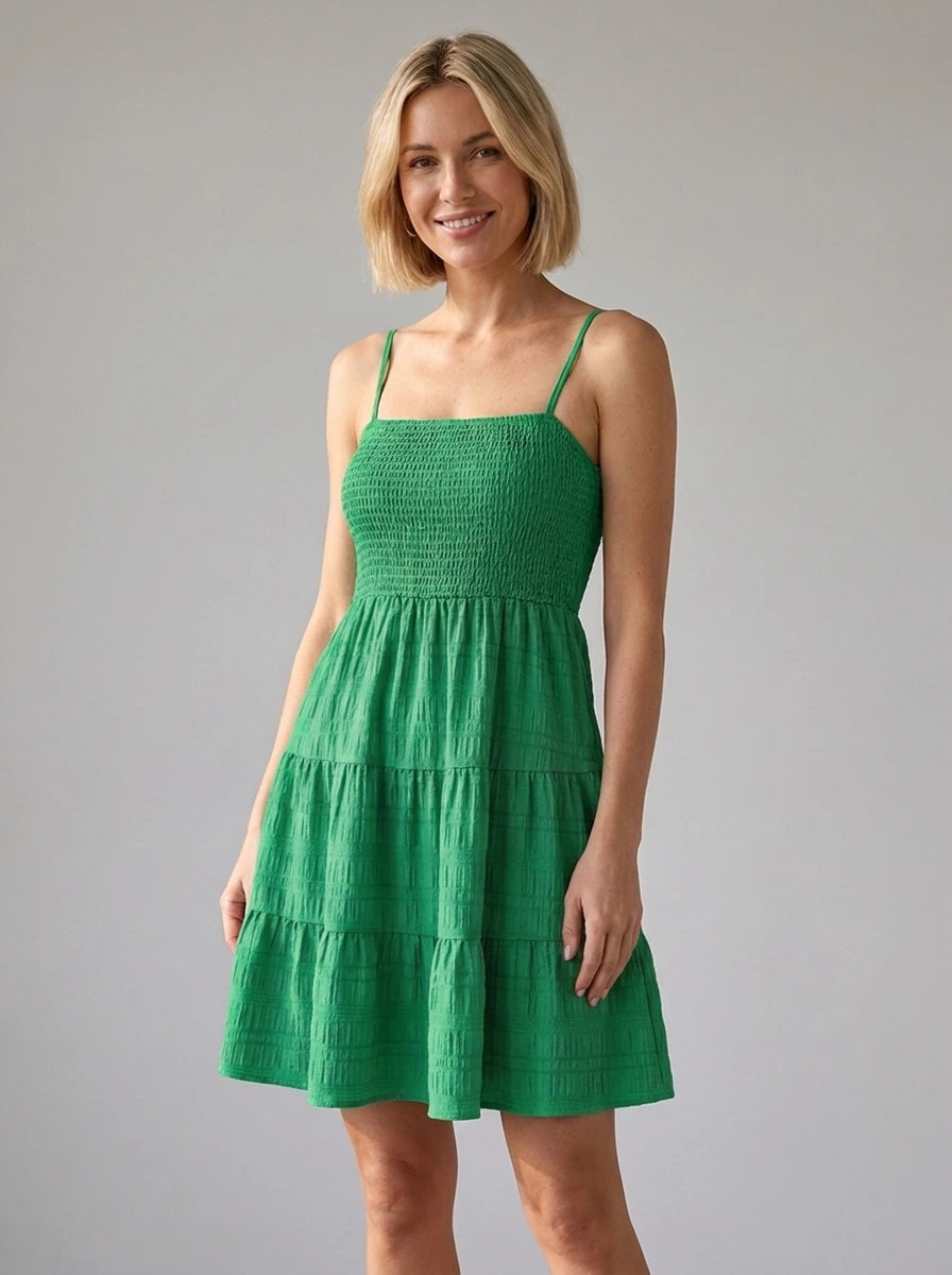 Woman wearing a green smocked tiered mini dress in a studio setting