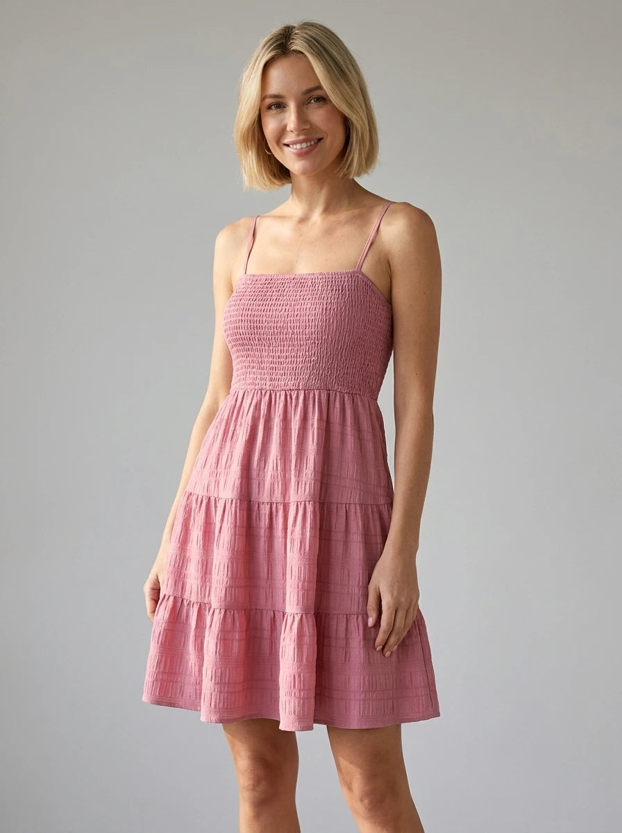 Woman wearing a pink smocked tiered mini dress in a studio setting