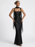 Woman wearing a black square neck ruched maxi dress with sheer wrap in a studio setting