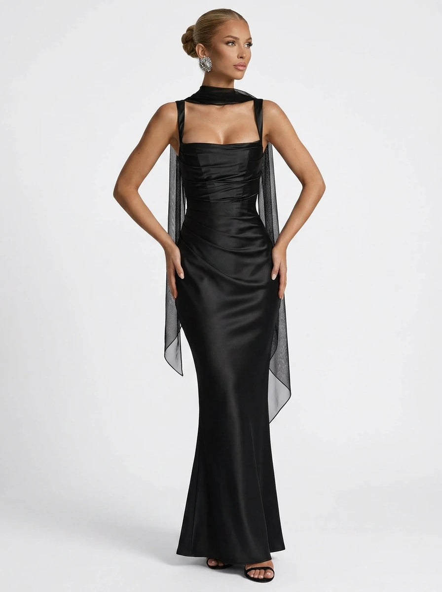 Woman wearing a black square neck ruched maxi dress with sheer wrap in a studio setting