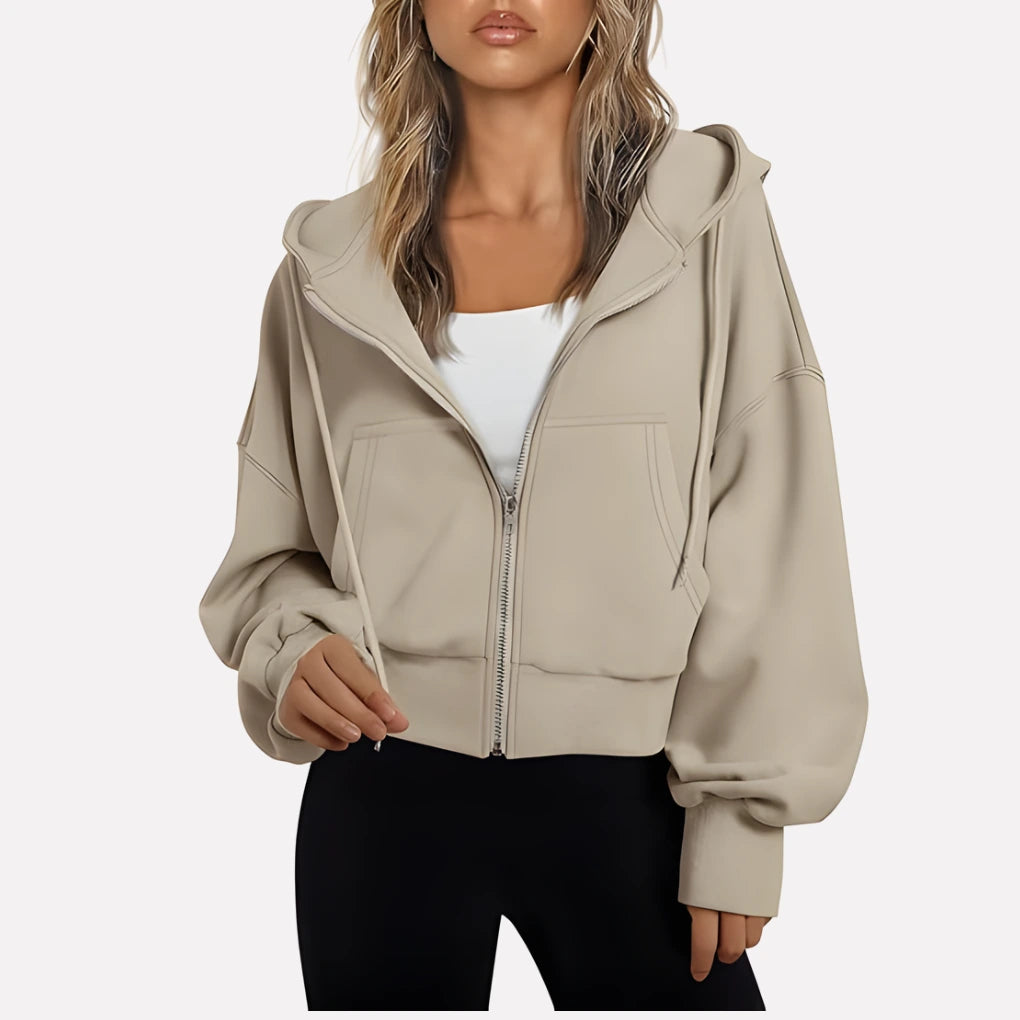 Woman wearing a beige cropped zip hoodie in a studio setting