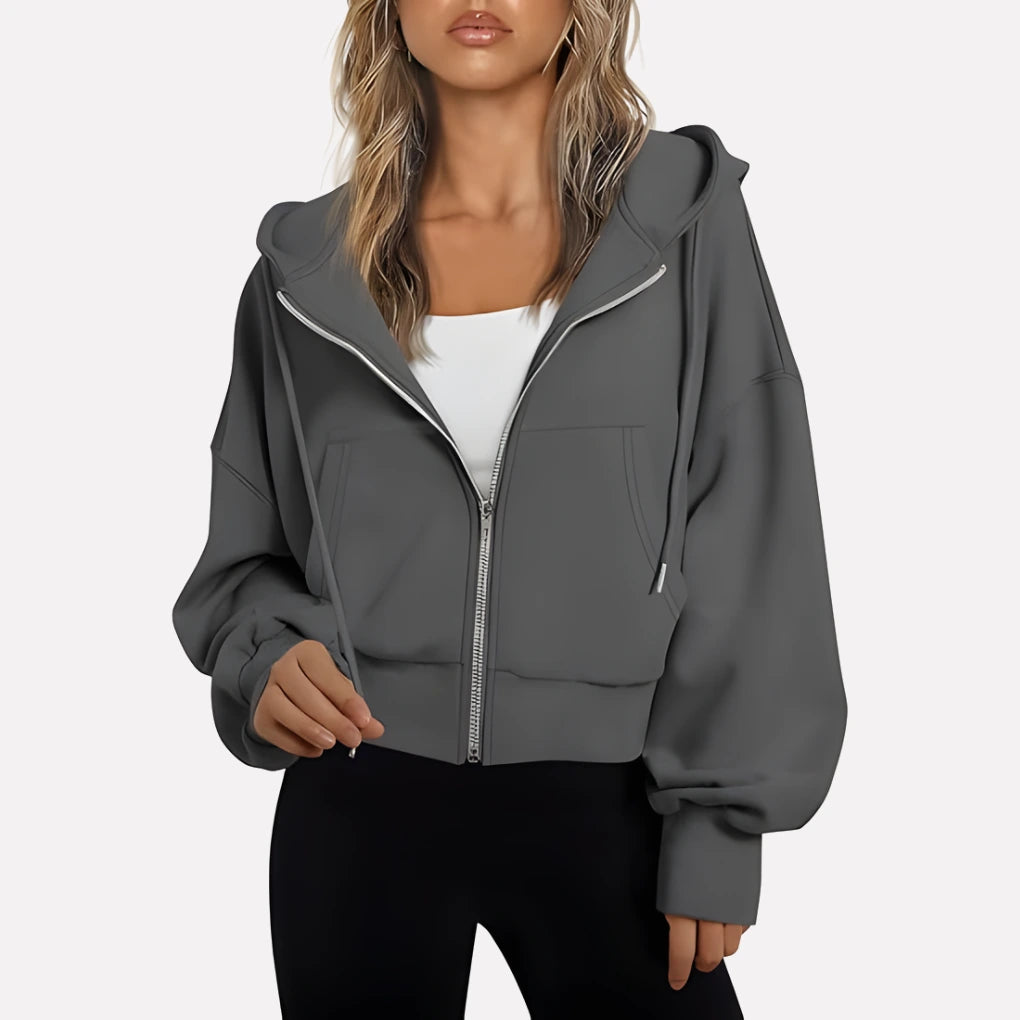 Woman wearing a dark grey cropped zip hoodie in a studio setting