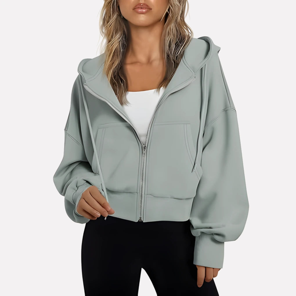Woman wearing a light grey cropped zip hoodie in a studio setting