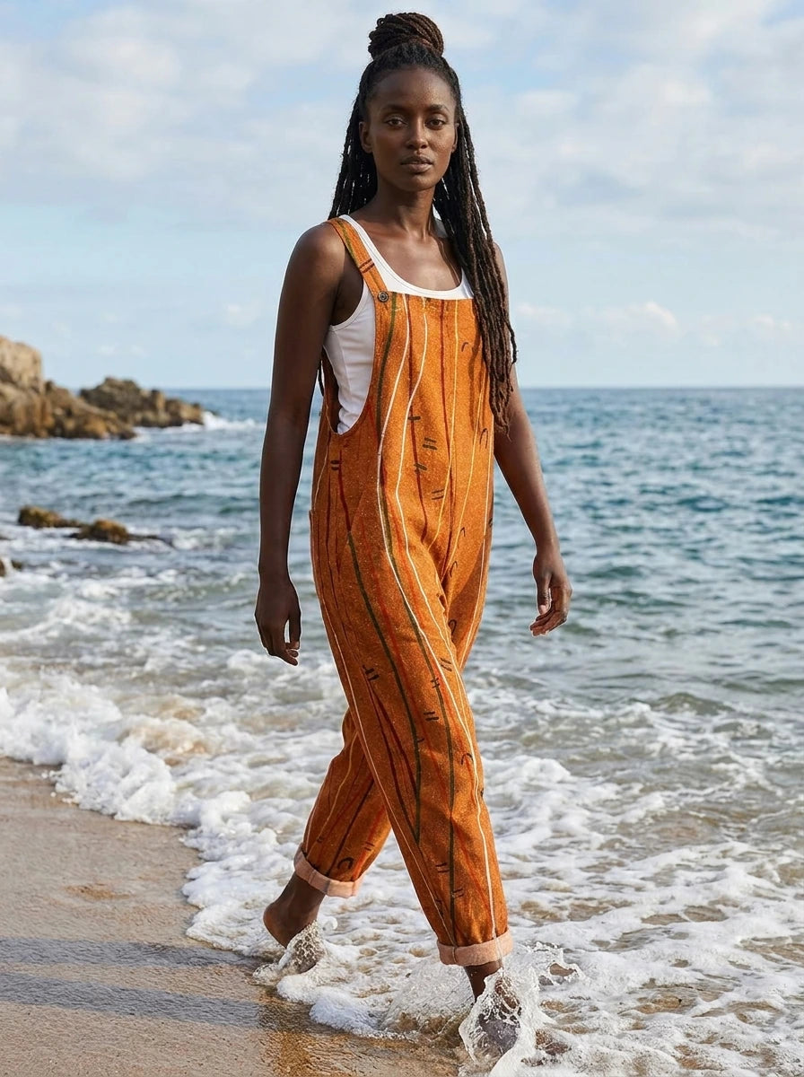 Woman in a rust-orange striped jumpsuit walking along the beach shoreline